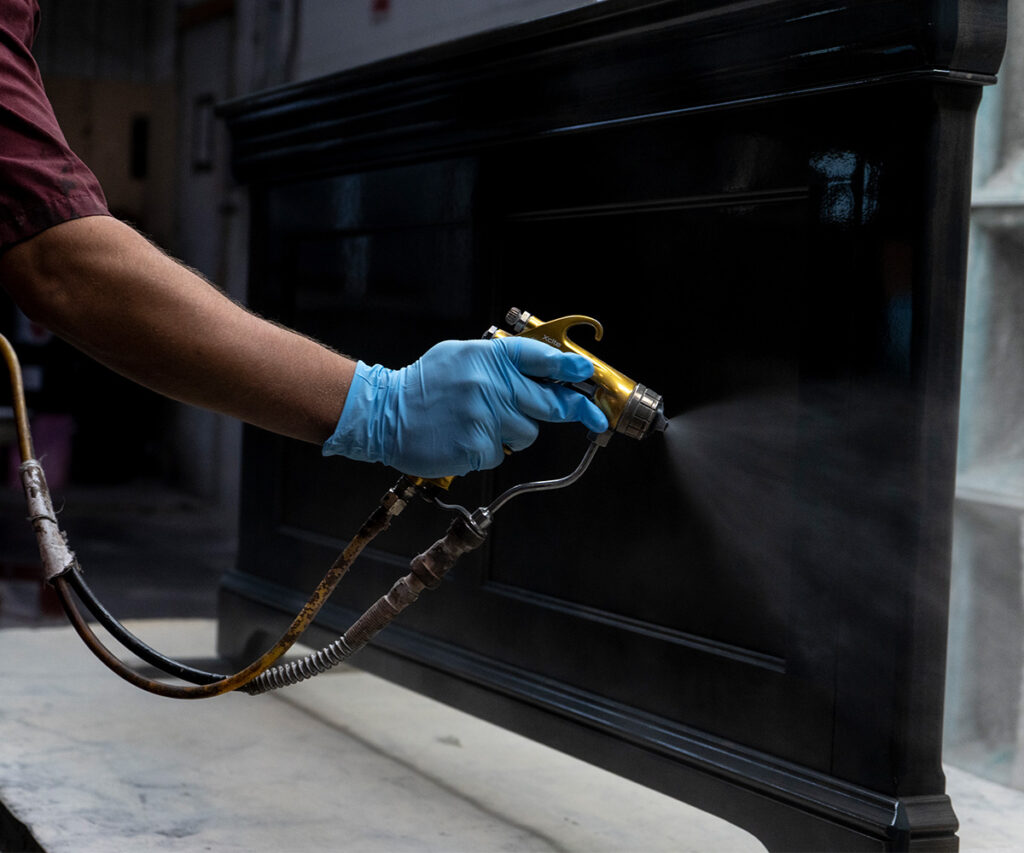 A man wearing blue latex gloves spraying a piece of furniture with black stain